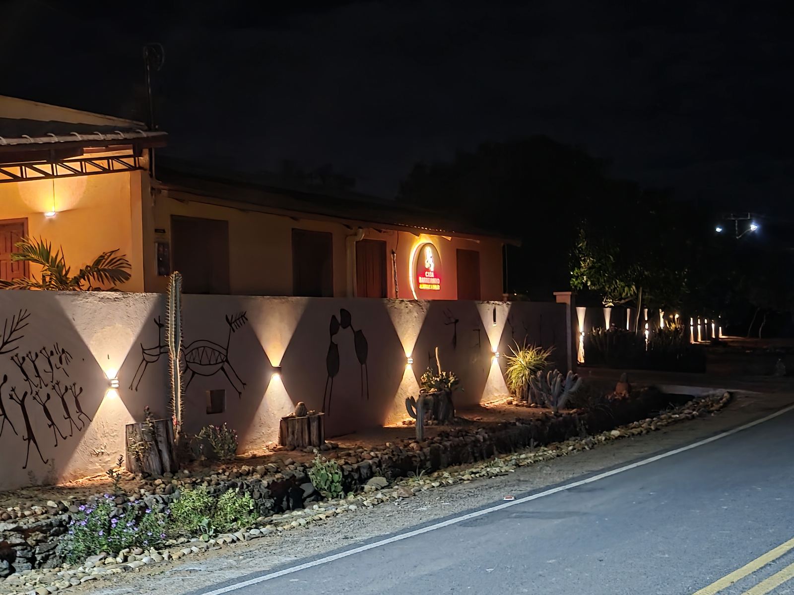 Casa Barreirinho à noite, com o muro iluminado decorado com motivos de pinturas rupestres